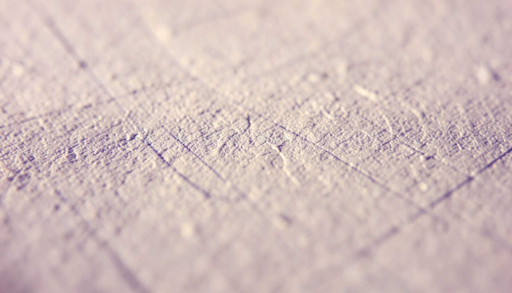 Extreme close-up photograph of a textured off-white paper surface with faint grid lines, warm natural light casting soft shadows that reveal the paper's fibrous grain